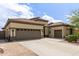 View of the tan home's three-car garage with a wide driveway and desert landscaping at 27315 N 83Rd Dr, Peoria, AZ 85383