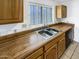 The kitchen features a stainless steel double sink, light wood cabinets, a wooden countertop and a window at 4247 N 101St Ave, Phoenix, AZ 85037