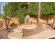 Charming backyard fireplace area with stone accents, seating, and mature trees, offering a cozy gathering space at 4223 N St Elias --, Mesa, AZ 85215