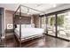 Spacious bedroom with a four-post bed, wood floors, brick accent wall and an adjacent balcony at 7740 E Heatherbrae Ave # 13, Scottsdale, AZ 85251