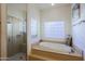 Bright bathroom featuring tile floors, glass block window, walk-in shower, and a luxurious soaking tub at 15954 W Sheila Ln, Goodyear, AZ 85395