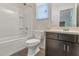 Bathroom featuring a single sink, dark cabinets, and a shower-tub combo with a white tiled surround at 2491 N 149Th Ln, Goodyear, AZ 85395
