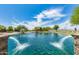Scenic pond view with decorative fountains and mature trees under a partly cloudy blue sky at 37384 W Prado St, Maricopa, AZ 85138