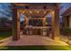 Outdoor kitchen with grill, mini fridge, and wooden pergola strung with decorative lighting at 1607 W Pearce Rd, Phoenix, AZ 85041