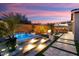 Inviting backyard with a pool, spa, outdoor kitchen, fire pit, and covered patio at dusk at 32268 N 133Rd Ln, Peoria, AZ 85383