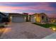 Charming home featuring a brick driveway, stone accents, two-car garage, and desert landscaping under a beautiful dusk sky at 32268 N 133Rd Ln, Peoria, AZ 85383