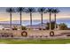 View of the Cobblestone Farms community entrance with lush landscaping and mature palm trees at 44566 W High Desert Trl, Maricopa, AZ 85139