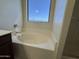 A clean and bright bathroom featuring a soaking tub beneath a window, perfect for relaxation at 12571 W Clarendon Ave, Avondale, AZ 85392