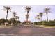 Gated community entrance featuring a tile roof covering, palm trees, and a beautifully landscaped median at 3306 E Jaeger Cir, Mesa, AZ 85213