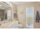 Bright bathroom featuring a single sink vanity and tiled shower behind glass doors and a window at 11113 W Cameo Dr, Sun City, AZ 85351