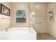 Well-lit bathroom showcasing a soaking tub, glass shower, and neutral-toned tiling at 4946 N 210Th Ave, Buckeye, AZ 85396