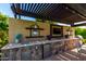 Outdoor kitchen featuring a built-in grill, sink, mini-fridge and entertainment center with a pergola covered patio at 17673 E Bronco Dr, Queen Creek, AZ 85142