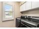 Bright laundry room featuring modern gray washer and dryer, white storage cabinets, and window at 7746 E Bisbee Rd, Scottsdale, AZ 85258