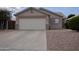 Tan single-story home with a spacious driveway and two-car garage, trimmed with stacked stone accents at 15351 W Port Royale Ln, Surprise, AZ 85379