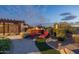 Backyard fire pit under pergola surrounded by lush landscaping and comfortable seating at twilight at 18438 N 96Th Way, Scottsdale, AZ 85255