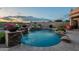 Backyard pool with rock waterfall feature, spa, lush landscaping, and comfortable seating under cloudy sunset sky at 18438 N 96Th Way, Scottsdale, AZ 85255