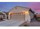 Beige home featuring a two-car garage, exterior lighting, and an ADT security system sign at dusk at 20555 N 261St Ave, Buckeye, AZ 85396