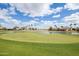 Manicured golf course with a green putting surface, surrounded by a picturesque lake, palm trees, and blue skies at 3910 N 163Rd Dr, Goodyear, AZ 85395