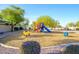 Community playground featuring a blue slide, yellow and red climbing structures, and spring riders amid lush greenery at 15796 W Shaw Butte Dr, Surprise, AZ 85379