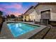 A serene in-ground pool shimmers under twilight skies, complemented by outdoor lighting and manicured landscaping at 16861 W Ironwood St, Surprise, AZ 85388