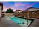 Twilight view of a sparkling in-ground pool surrounded by concrete, with lights and a colorful sunset at 16861 W Ironwood St, Surprise, AZ 85388