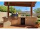 An outdoor kitchen area with a stainless steel grill, cabinets, and a mini-fridge on a tiled patio offers space for al fresco dining at 2449 E Desert Flower Ln, Phoenix, AZ 85048