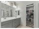 Well-lit bathroom featuring a dual-sink vanity, large mirror, and a glimpse into an organized walk-in closet at 12374 W Locust Ln, Avondale, AZ 85323