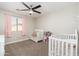 Neutral-toned bedroom with two cribs, carpet, a window with light pink curtains, and a modern ceiling fan at 14095 W Larkspur Dr, Surprise, AZ 85379