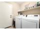 Well-lit laundry room with white washer and dryer units, a white door, and storage shelves at 553 W Hereford Dr, San Tan Valley, AZ 85143