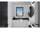 Well-lit laundry room with white cabinets, countertop, and stacked washer and dryer under a window at 5814 E Camelback Rd, Phoenix, AZ 85018