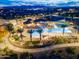 Aerial view of the community pool area featuring a splash pad, lounge chairs, and palm trees with city lights in the background at 15911 W Montana De Oro Dr, Surprise, AZ 85387