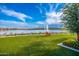 Beautiful lake view with chairs on green grass, featuring a calm lake with a fountain, clear blue skies, and distant homes at 17244 W West Wind Dr, Surprise, AZ 85387