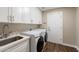 Well-equipped laundry room with modern white cabinetry, sink, counter and front-load washer and dryer at 14424 N 64Th Pl, Scottsdale, AZ 85254