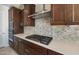 Close-up of cooktop, herringbone backsplash and stainless vent over dark wood cabinetry at 21278 N 272Nd Ave, Buckeye, AZ 85396