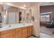Bathroom with double sinks, wood cabinets and a large mirror is attached to another room in the house at 18058 W Weatherby Dr, Surprise, AZ 85374