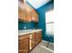 A bright laundry room with blue walls, light wood cabinets, a utility sink, and a window at 27083 W Marco Polo Rd, Buckeye, AZ 85396