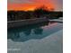 Beautiful pool reflecting a vibrant sunset, surrounded by a stone patio and lush landscaping at 27083 W Marco Polo Rd, Buckeye, AZ 85396