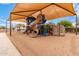 Community playground featuring a large, covered play structure with slides and climbing walls on a sandy base at 41227 W Granada Dr, Maricopa, AZ 85138