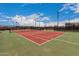 Immaculate community tennis court featuring red clay surface with netting under clear blue sky, perfect for tennis enthusiasts at 41227 W Granada Dr, Maricopa, AZ 85138