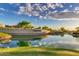 Scenic community entrance featuring a pond with lush landscaping under a bright, cloudy sky at 17139 S 174Th Dr, Goodyear, AZ 85338