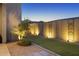 Lush backyard featuring uplighting, artificial grass, and a privacy wall with decorative metal artwork at 948 E La Mirada Dr, Phoenix, AZ 85042