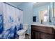 Charming bathroom with blue accent wall, wooden vanity, toilet, and shower with a decorative curtain at 10561 E Plata Ave, Mesa, AZ 85212