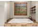 Inviting bathroom showcases soaking tub beneath a window, wooden shelves, and tiled accents for relaxation at 2335 E Allen St, Phoenix, AZ 85042