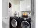 Laundry room with full-size black washer and dryer units and cabinet at 7506 N 47Th Dr, Glendale, AZ 85301