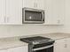 Close-up of a kitchen featuring granite counters, stainless steel microwave, and black gas range at 37112 W Prado St, Maricopa, AZ 85138