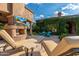 Cozy outdoor space with a fireplace, lounge chairs, a dining table, and lush landscaping at 16469 N 113Th Way, Scottsdale, AZ 85255