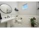 Elegant powder room with pedestal sink, round mirror, and black and white tile flooring at 20213 W Amelia Ave, Buckeye, AZ 85396