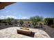 Beautiful backyard patio featuring a modern gas fire pit, desert landscaping, and views of the lush green golf course at 26421 W Zachary Dr, Buckeye, AZ 85396