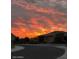 Serene street view with a vibrant sunset backdrop, featuring well-maintained homes and desert landscaping at 26421 W Zachary Dr, Buckeye, AZ 85396