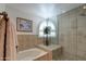 Bright bathroom featuring a glass-enclosed shower, soaking tub, shuttered window, and neutral tile at 7015 W Behrend Dr, Glendale, AZ 85308